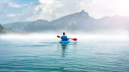 Man with kayak on a misty lake in front of big mountains