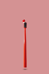 Single red toothbrush with red and white Santa hat floating on pink background with copy space. Dental medical Christmas and New Year concept. Creative medical health still life levitation.
