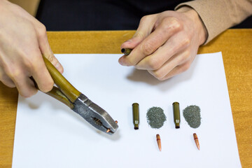 Men's hands with pliers pull out a bullet from a cartridge case