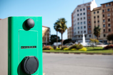 Detail of electric car charging station with a square city environment like a background.