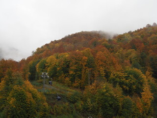 A modern cable car rides into the mountains, with cloudy sky in the background. Beautiful view of the cable car in autumn.