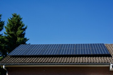 Fototapeta premium House with solar panels covering its tiled roof under a clear blue sky on a sunny day