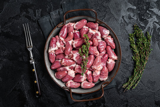 Raw chicken hearts in a steel tray with thyme. Black background. Top view