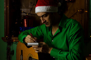 Handsome man sitting at home alone at Christmas, playing on guitar and writing new music at night...
