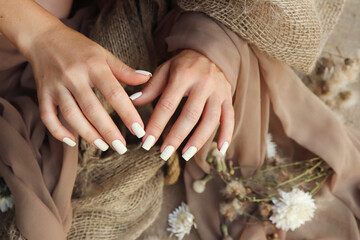 Nail extensions with light beige gel polish on short square nails with flowers and decor.