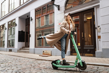 Young blonde woman riding a kick scooter in city street