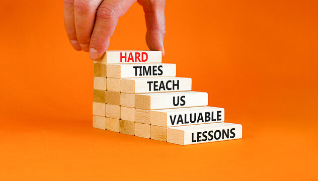 Lesson from hard times symbol. Concept words Hard times teach us valuable lessons on wooden blocks on a beautiful orange background. Businessman hand. Business lesson from hard times concept.