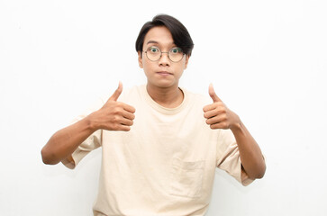 asian young man in casual beige tshirt pointing finger showing something good. man with glasses shocked happily pointing up with copy space isolated over white background. advertisment model concept.