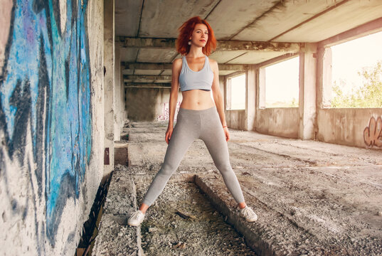 Fitness woman in sportswear doing stretching exercise on city street over gray concrete background. Outdoor sports clothing and shoes, urban style.