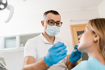 Fototapeta premium Consultation with dentist at dentistry. Teeth treatment. Dentist examines girl mouth and teeth and treats toothaches. Happy woman patient of dentistry.