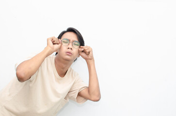 Young Asian man wearing glasses and beige tshirt with crying face expression isolated over white background. Crying face expression of Young Asian man with hand gesture. 