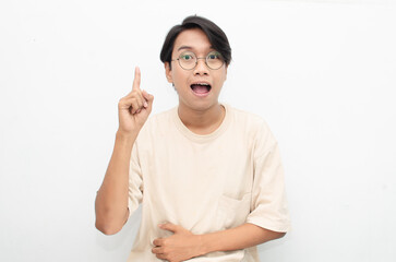 asian young man in casual beige tshirt pointing finger showing something good. man with glasses shocked happily pointing up with copy space isolated over white background. advertisment model concept.