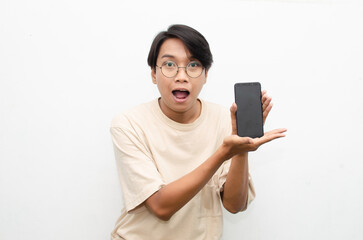 excited young asian man in beige tshirt holding and showing phone screen with happy euphoric...