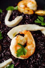delicious black rice with shrimps and seafood on a black wooden rustic background