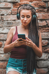 Fototapeta premium Woman With Long Afro Braided Hair Listening Music From A Headphones Outdoor