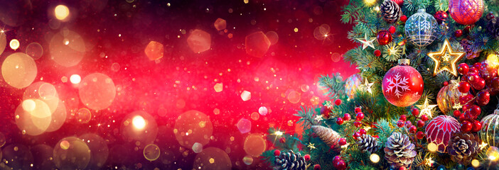Weihnachtsbaum im roten glänzenden Hintergrund - Verzierungen auf Tannenzweigen mit glitzernden und defokussierten abstrakten Lichtern