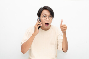 excited young asian man in beige tshirt holding and showing phone screen with happy euphoric shocked wow expression. man pointing to screen phone with thumb up. billboard model advertisment concept.
