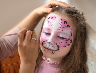 Cute makeup little tiger. face painting outdoors, having fun, copy space. girl with aqua makeup of tiger muzzle. Master making aqua makeup on girl face. aqua grimm on birthday or halloween party