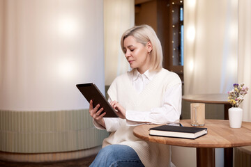 A cute girl is sitting with a tablet and a diary in a cafe and drinking coffee