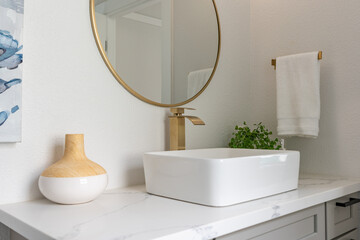 Modern bathroom vanity details of gold faucet with raised basin and decorative gold-trimmed mirror.