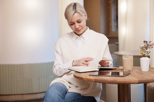 Cute girl in a shirt flipping through a diary in a cafe