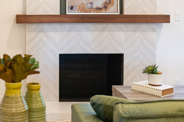 Modern fireplace view over couch of patterned tile facing, wood bean mantle, and green accents...