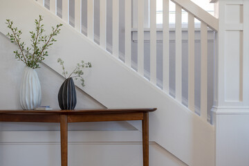 Contemporary detail of interior staircase with natural wood table and two decorative vases.