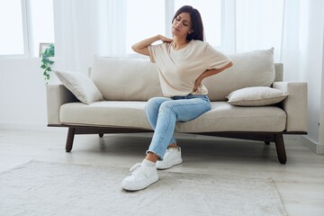 Fototapeta premium Woman sitting on sofa at home back and lower back pain, protrusion, back problems after 30 years