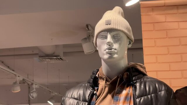 Male mannequin in a brown down jacket and a stocking cap or slouchy beanie stands in the window of a clothing store