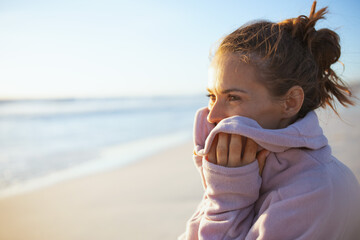 stylish woman in cosy sweater at beach in evening relaxing