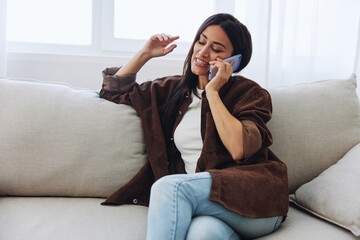 Woman blogger with phone lying at home and talking on the phone on sofa with laptop and working freelancer online, smiling with teeth