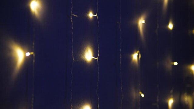 The lights of the garland lighting up and going out in the wall. Abstract blurred lights sparkling and glowing on black background. Christmas or New Year holiday concept.