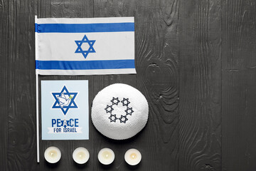Flag of Israel, kippah, burning candles and card with text PEACE FOR ISRAEL on dark wooden background