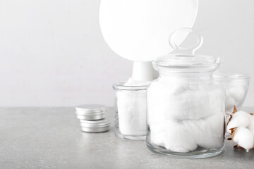 Containers with soft cotton wool on table near light wall