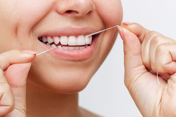 Close-up of a young woman flossing her teeth after meal on white background. Dental health care,...