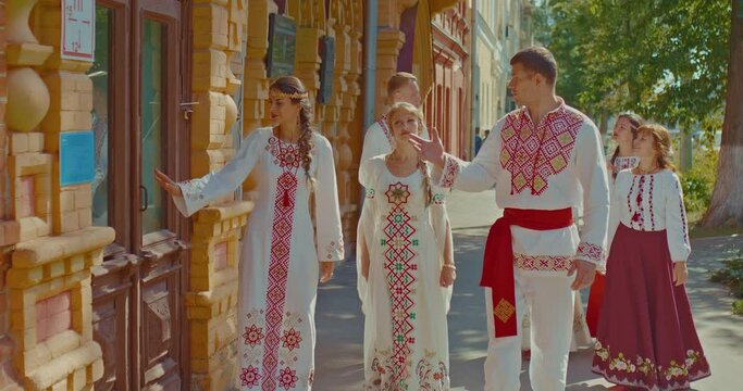 Slavic men and women in beautiful national costumes walk around the city and talk. Pretty women in folk dresses with embroidery, men in embroidered shirts. Happy people, friendship of peoples. 4k
