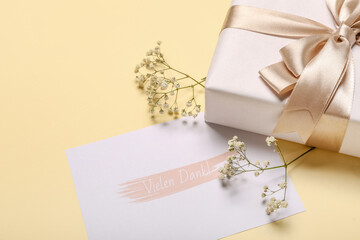 Card with text VIELEN DANK, flowers and gift box on beige background
