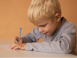 Little boy with hearing aid write book indoors