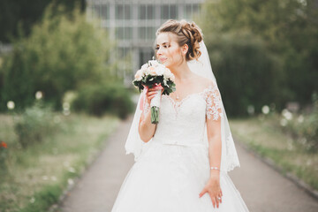 Fototapeta na wymiar Beautiful bride in elegant white dress holding bouquet posing in park
