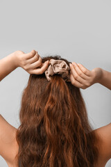 Naklejka premium Woman adjusting silk scrunchy on light background
