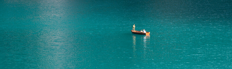 Three people are having fun on a wooden boat. Take a mobile selfie. Blue water. Beautiful nature. Lake Braies. Italy. Dolomites. People in a beautiful place