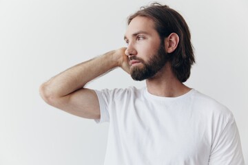 Portrait of a man with a black thick beard and long hair in a white T-shirt on a white isolated background emotion of sadness and longing