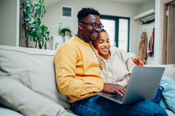 Multiracial couple using laptop while sitting on a sofa at home
