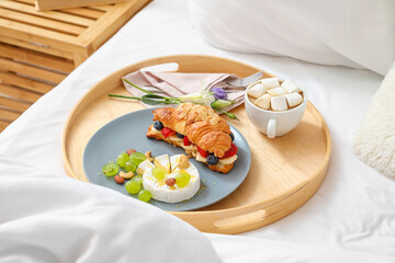 Wooden tray with tasty breakfast and cup of cacao on bed