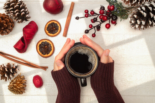 Hands holding coffee with sweater pulled over to keep warm with holiday theme