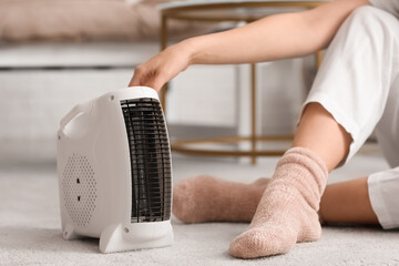 Modern electric fan heater and woman in warm socks on carpet, closeup