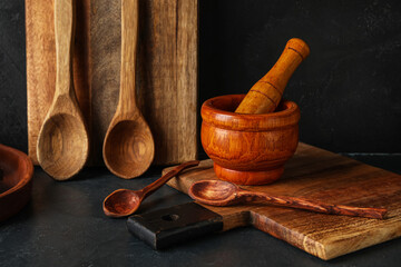 Wooden cutting boards, mortar with pestle and spoons on black background