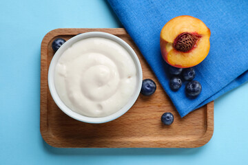 Board with bowl of pudding, peach, blueberries and napkin on color background, closeup