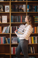 Teen girl among a pile of books. A young girl holding books with shelves in the background. She is surrounded by stacks of books. Book day. © arthurhidden
