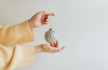 A woman in a yellow sweater is holding a blue embossed Christmas tree ball in her hands.